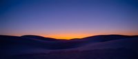 Twilight desert landscape with rolling sand dunes silhouetted against vibrant orange and purple sunset sky, suitable for travel and nature backgrounds.