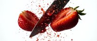 Fresh strawberry being sliced with knife creating dynamic splash of juice and seeds on white background for culinary design projects.