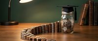 Young professional saving money for education with coins in glass jar and graduation cap on wooden desk with books and lamp in warm lighting.
