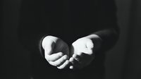 Business professional in formal suit extending cupped hands in gesture of offering, receiving or protection against dark background.