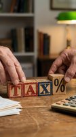 Senior male accountant arranging wooden tax blocks on desk with calculator and documents, representing financial planning, accounting services, and tax preparation for business and personal finance.