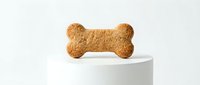 Dog bone-shaped biscuit treat displayed on white cylindrical pedestal against neutral background, suitable for pet food packaging and veterinary marketing materials.