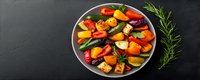 Colorful roasted vegetables with bell peppers, zucchini, and fresh herbs served on gray plate against dark background, healthy Mediterranean cuisine.