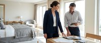 Professional businesswoman and businessman reviewing documents and plans in modern hotel room during business meeting or property inspection.