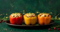 Three colorful stuffed bell peppers with rice and herbs on dark plate, festive holiday dinner preparation with Christmas decorations and warm lighting.