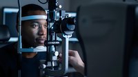 African American woman undergoing comprehensive eye examination using advanced slit lamp biomicroscope equipment in modern ophthalmology clinic setting.