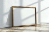 Empty wooden picture frame leaning against white wall on wooden floor with natural window light and shadows, mockup for artwork presentation.