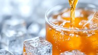 Golden liquid pours into glass with ice cubes creating refreshing drink splash, close up view against blurred background with bokeh effect.