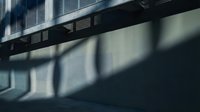 Dramatic shadows cast by metal railing create geometric patterns on concrete wall, showcasing interplay of light and architecture in urban setting.