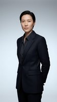 Professional Asian businesswoman in dark suit standing confidently against gray background for corporate and business presentations.