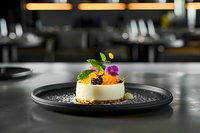 Elegant dessert plated on black ceramic dish featuring creamy white mousse topped with citrus segments, edible flowers, and fresh herbs in upscale restaurant setting.