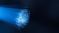 Blue fiber optic cables with glowing light particles streaming through dark background for technology and communication concepts.