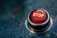 Red illuminated stop button on dark textured background with selective focus and bokeh effect, dramatic lighting creates emergency or control panel mood.