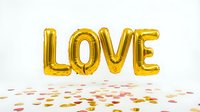 Gold foil letter balloons spelling LOVE floating above colorful heart confetti on white background, perfect for Valentine's Day and celebrations.