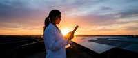 Female engineer using tablet at solar panel farm during golden hour sunset for renewable energy monitoring and maintenance operations.