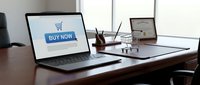 Open laptop displaying a buy now button with shopping cart icon on desk beside miniature cart and certificate for e-commerce concept.