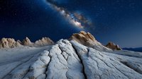 Dramatic white sandstone formations under starry night sky with Milky Way galaxy stretching across horizon, creating otherworldly desert landscape at twilight.