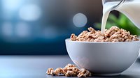 Pouring milk into white ceramic bowl with crunchy chocolate breakfast cereal against blurred background, morning nutrition concept, macro food photography.