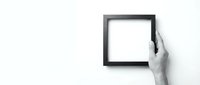 Hand holding empty black picture frame against white wall for mockup and design projects.