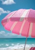 Pink beach umbrella with water drops against turquoise ocean and blue sky with white clouds, creating summer vacation atmosphere at seaside resort.