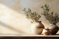Rustic ceramic vases with fresh olive branches on wooden shelf against beige wall with natural sunlight and shadow creating minimalist home decor composition.