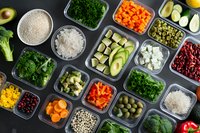 Fresh ingredients in meal prep containers with quinoa, rice, vegetables, legumes and fruits arranged on dark background for healthy eating and balanced nutrition.