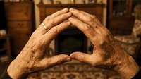 Elderly hands forming protective shelter gesture in warm home interior, symbolizing care, security and family protection concepts.