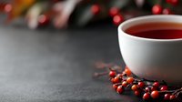 Hot herbal tea in white cup with red berries on dark surface, cozy winter drink for cold weather and seasonal wellness rituals.