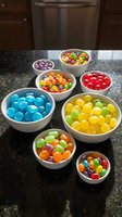 Colorful candy assortment in white bowls on granite counter, featuring jelly beans, gumballs and sweets sorted by color for party planning and dessert displays.