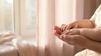 Woman practicing meditation with hands in mudra position by sunny window with soft pink curtains creating peaceful morning wellness atmosphere.