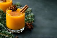 Fresh pumpkin spice smoothie garnished with cinnamon stick and star anise on dark background with pine branches, winter warming beverage.