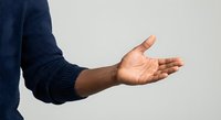 African American man in navy sweater extending open palm in welcoming gesture against neutral background for business presentations.