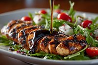 Grilled chicken breast sliced on fresh arugula salad with cherry tomatoes and mozzarella, drizzled with balsamic glaze for healthy meal option.