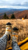 Cozy knitted socks with deer pattern against mountain landscape and camping tent background, relaxing in hammock during autumn outdoor adventure.