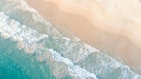 Aerial view of turquoise ocean waves washing onto pristine sandy beach shore creating white foam patterns on tropical coastline for travel content.