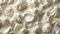 Creamy white whipped cream swirls and peaks create luxurious texture background with soft shadows and delicate patterns, fresh dairy dessert topping closeup.