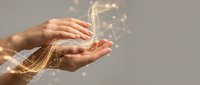 Human hands cupping glowing digital network connections with golden light particles floating above palms representing innovation and technology concepts.