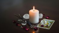 Mystical fortune telling setup with burning candle, tarot cards, crystals and pendulum for spiritual guidance and divination practices.
