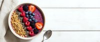 Acai smoothie bowl topped with fresh berries, granola, and chia seeds on a white wooden table, healthy breakfast concept.