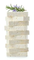 Stacked artisanal soap bars with lavender and rosemary herbs on top, isolated on white background for cosmetic product packaging and wellness branding.