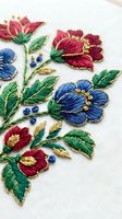 Colorful hand embroidered floral design with red and blue flowers on white fabric showcasing traditional needlework craftsmanship for textile and craft projects.