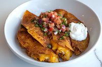 Crispy corn tortillas filled with seasoned meat and melted cheese, topped with fresh pico de gallo and sour cream, served in white ceramic bowl for Mexican cuisine.