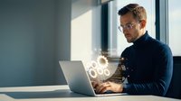 Young Caucasian businessman in glasses working on laptop with digital network connections in modern office environment for technology concepts.