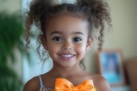 Young girl with curly hair and warm smile holding orange fruit, perfect for family, health, nutrition, and children's lifestyle content.