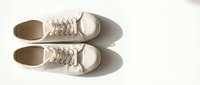 Pair of white canvas sneakers with laces on a light background, top view with natural shadow, minimalist style for fashion and lifestyle concepts.