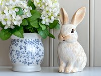 White ceramic bunny figurine next to blue and white porcelain vase with fresh white hydrangea flowers on light gray surface, elegant home decor arrangement.