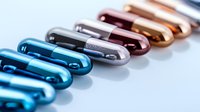 Metallic capsule pills in vibrant colors arranged in diagonal line on white background, pharmaceutical concept with blue, silver, and rose gold tones.