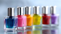 Colorful nail polish bottles in row on reflective surface with blue, pink, orange, yellow, red and purple shades against light background. Perfect for beauty and cosmetics.