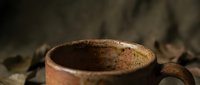Rustic ceramic coffee mug with speckled brown glaze on wooden surface with warm atmospheric lighting for cozy morning beverage moments.