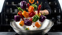 Fresh colorful bell peppers falling into metal bowl with ice and water splashes in modern kitchen for healthy cooking and meal preparation.